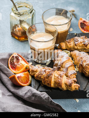 Petit-déjeuner maison traditionnelle de style italien. Latte dans les verres, des croissants aux amandes et oranges siciliennes sanglant rouge sur tableau texturé en béton Banque D'Images