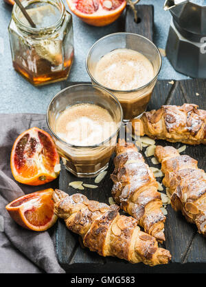 Petit-déjeuner maison traditionnelle de style italien. Latte dans les verres, des croissants aux amandes et oranges siciliennes sanglant rouge sur tableau texturé en béton Banque D'Images