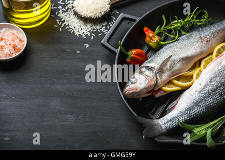 Le bar cru Raw fish de fines herbes, d'épices et le riz en casserole en fonte noire sur fond de bois Banque D'Images