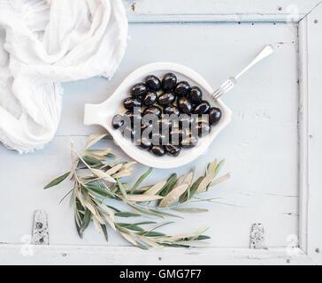 Olives noires dans la plaque en céramique blanche avec des branches d'arbre, vue du dessus Banque D'Images