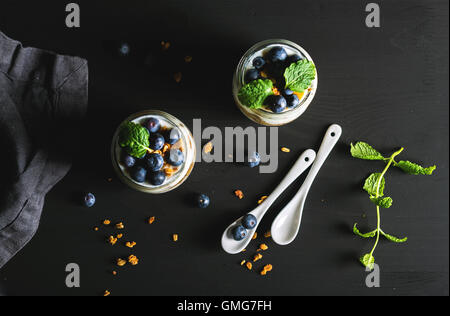 Petit-déjeuner sain. Yaourts aux myrtilles granola avoine et de feuilles de menthe dans des bocaux en verre sur fond noir Banque D'Images