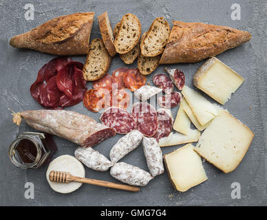 Du fromage et de la viande ou du vin sélection de hors-jeu de casse-croûte. Variété de fromage, salami italien, bresaola, baguette, plus de miel sur fond de béton gris, vue du dessus. Banque D'Images