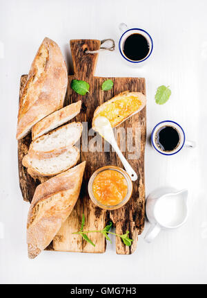 Le petit-déjeuner ensemble. Baguette, confiture d'orange et du café dans des gobelets en bois rustique sur office sur fond peint en blanc Banque D'Images