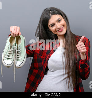 Happy woman holding retro sneakers contre l'arrière-plan gris Banque D'Images