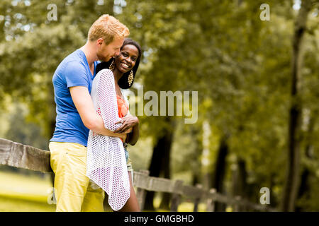 Jeune couple multiracial dans l'amour debout à côté de la clôture dans le parc sur une journée ensoleillée