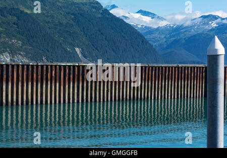 Un mur sépare la mer crénelées rouillé sa réflexion et d'une colline boisée à Whittier en Alaska. Banque D'Images
