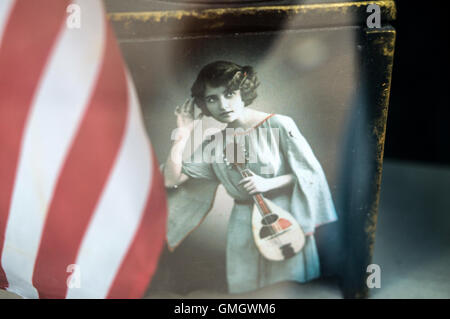 Une femme des années 1920 en costume tenant une mandoline contient jusqu'sa main d'écouter de la musique à côté du drapeau américain Banque D'Images