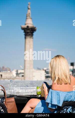 Portrait d'une femme vertical sirotant un cocktail donnant sur la Colonne Nelson à Trafalgar Square, Londres, au soleil. Banque D'Images