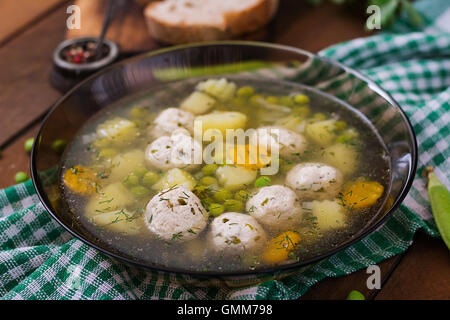 Soupe diététique avec du poulet et boulettes de petits pois dans un bol en verre sur un fond de bois. Banque D'Images