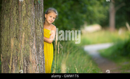 Little girl peeking de derrière l'arbre. Banque D'Images