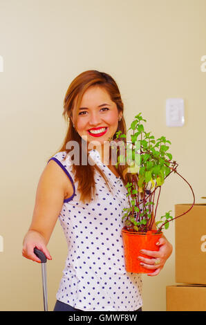 Happy young woman holding plante verte et de saisir la poignée de valise avec les autres, se déplaçant en concept Banque D'Images