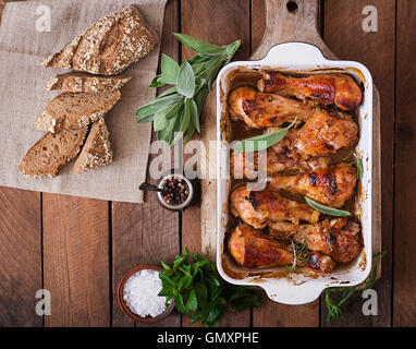 Appétissants pilons de poulet doré au four dans un plat allant au four, sur une table en bois. Vue d'en haut Banque D'Images