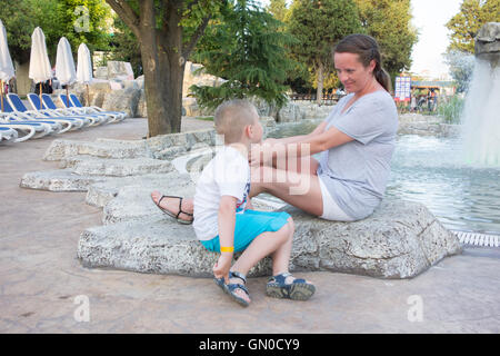 La mère et le fils assis sur un rocher et parler à la fontaine Banque D'Images