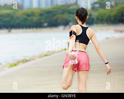 Young Asian woman runner stretching jambe dans un parc de la ville, vue arrière. Banque D'Images