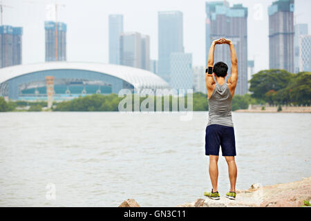 Les jeunes hommes asiatiques jogger avec fitness tracker attaché au bras de préchauffage en étirant les bras et haut du corps avant l'exécution, la ville s Banque D'Images