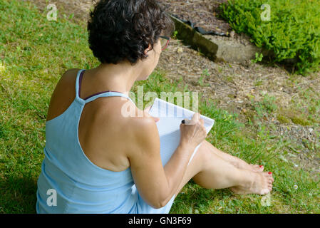 Belle femme mature écrit une lettre dans le jardin Banque D'Images
