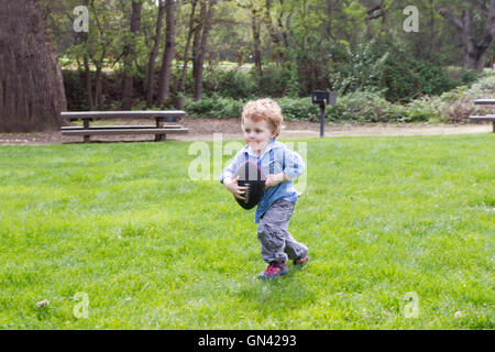Les jeunes trois ans caucasien boy running with football in park. Banque D'Images