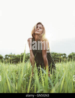 Portrait of attractive young dame assise dans le domaine de l'herbe un jour d'été. Portrait modèle féminin dans la prairie avec Banque D'Images