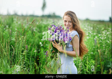 Belle jeune femme avec un bouquet de fleurs sur la prairie d'été Banque D'Images