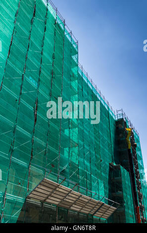 Bâtiment moderne est en construction, des échafaudages métalliques avec couverture réseau vert sur fond de ciel bleu. Banque D'Images