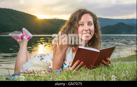 Jeune femme lisant un livre par le lac. Relaxation Solo Banque D'Images