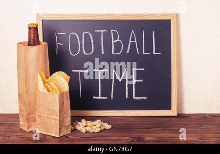 Les fans de football, concept de bouteille de bière dans le sac en papier brun, chips, pistaches et de l'écriture texte écrit en chalkbo temps football Banque D'Images