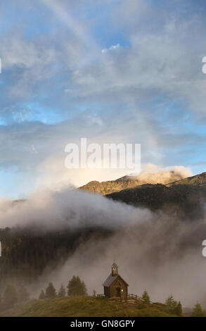 Les Dolomites, Trentino, en Italie. Un arc-en-ciel au-dessus de la petite chapelle en bois donnant sur Passo di Valles sur l'Alta Via 2 sentier, au lever du soleil en été Banque D'Images