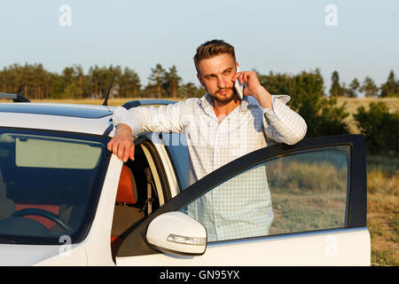 Beau jeune homme ouvrit la porte de sa voiture. L'homme au téléphone. Toujours connecté. Banque D'Images