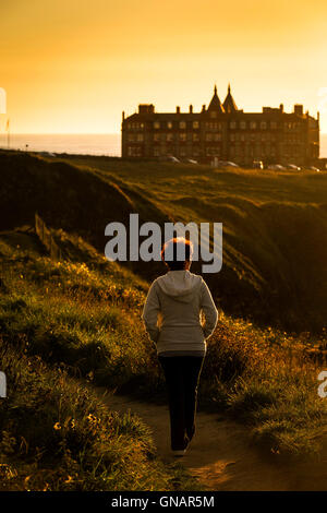 Une femme marche le long d'un chemin durant un intense coucher de soleil sur la Pointe à Newquay, Cornwall. Banque D'Images