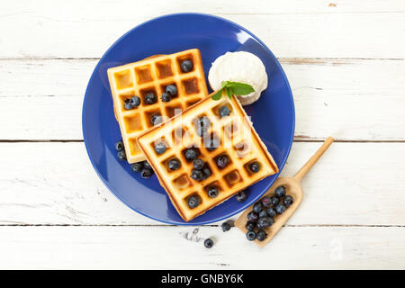 Gaufres Belges aux myrtilles et glace vanille scoop sur plaque bleue, sur une table en bois rustique, vue du dessus Banque D'Images