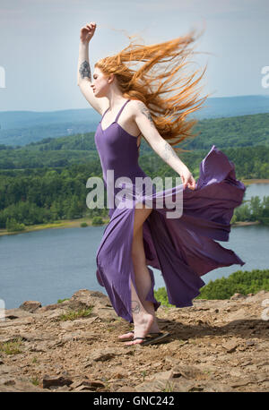 Portrait dramatique de belle tête rouge femme en robe pourpre, en montagne avec le vent dans les cheveux et un lac ci-dessous. Banque D'Images