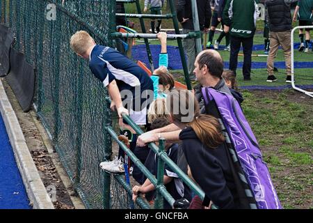 Champ de joueurs de hockey junior qui regarde un match de hockey de derrière une clôture, avec leur entraîneur. Banque D'Images