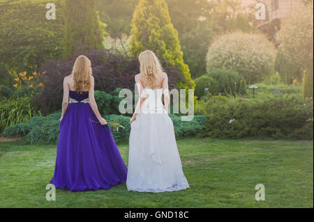 Mariée de demoiselle d'honneur et de l'extérieur. Deux jeunes filles posant sur le pré vert. Deux filles debout dos à la caméra. Mariée en robe de mariage. B Banque D'Images