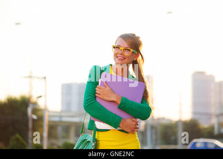 Fille d'affaires avec répertoire dans ses mains. Veste fille dans les verres et les sourires et regarde ailleurs. Banque D'Images