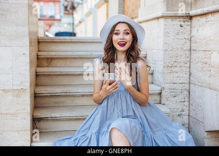 Young beautiful smiling woman in hat faire avec selfies smartphone outdoors Banque D'Images