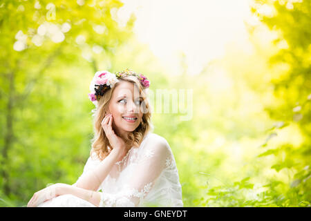 Mariée en robe de mariage avec couronne de fleurs, vert nature. Banque D'Images