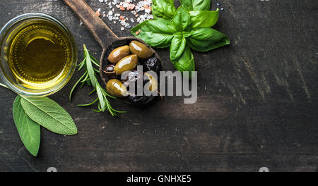 Olives vertes et noires dans la cuisine méditerranéenne vieille cuillère d'huile d'olive et d'herbes plus rustique en bois sombre, vue de dessus, l'arrière-plan Banque D'Images