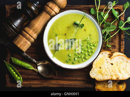 Soupe crème de pois fraîches faites maison dans un bol blanc avec le pain grillé sur planche de bois sur fond noir, vue du dessus, composition horizontale Banque D'Images