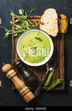 Soupe crème de pois fraîches faites maison dans un bol blanc avec le pain grillé sur planche de bois sur toile noir ardoise, vue du dessus, vertic Banque D'Images