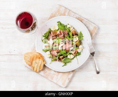 Le prosciutto, roquette, basilic, salade de mozzarella figues et servi avec des tranches de pain rustique sur carte avec verre de vin rouge sur blanc Banque D'Images