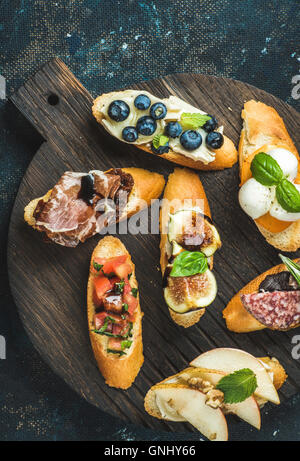 Crostini italiens avec divers nappages sur table ronde en bois servant au fond de contreplaqué noir, vue du dessus Banque D'Images