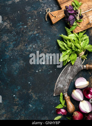 Arrière-plan de cuisson des aliments sains. Frais vert et de feuilles de basilic pourpre, oignons rouges et l'ail, d'herbes et de couteau hachoir cutti rustique Banque D'Images