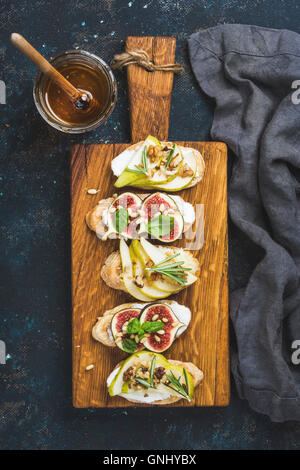 Crostini avec ricotta, poire, miel, figues, noix et herbes. Petit-déjeuner toasts ou sandwichs snack sur planche de bois rustique ove Banque D'Images