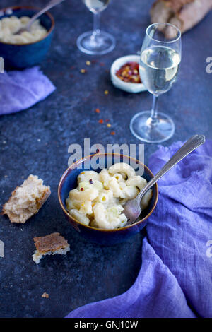 Artichauts crémeux Mac 'N' Cheese dans des bols en céramique servi avec du vin blanc et du pain. Photographié à partir de la vue de face sur un fond noir et Banque D'Images