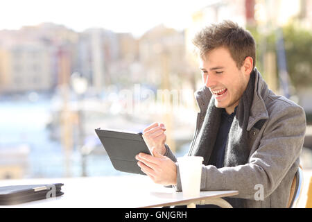 Beau vainqueur euphorique qui gagne et regardant un comprimé dans un café terrasse d'un port de l'urbanisation Banque D'Images