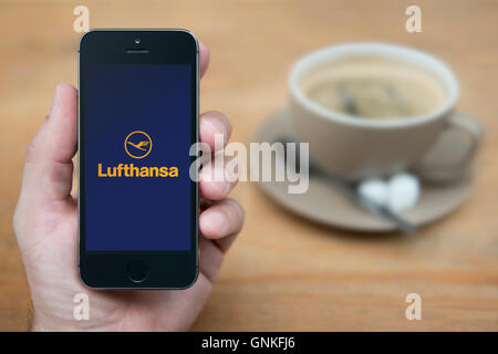 Un homme se penche sur son iPhone qui affiche le logo de Lufthansa, en restant assis avec une tasse de café (usage éditorial uniquement). Banque D'Images