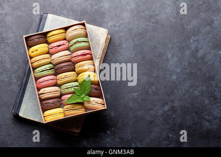 Macarons colorés dans une boîte-cadeau plus de livre sur table en pierre. Macarons sucrés. Vue de dessus avec l'exemplaire de l'espace pour votre texte Banque D'Images