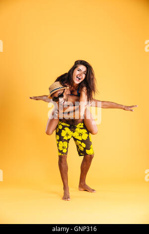 Young happy couple enjoying piggyback ride isolé sur fond orange Banque D'Images