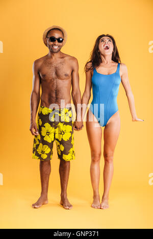 Belle jeune couple aimant en tenant les mains de beachwear isolé sur fond orange Banque D'Images