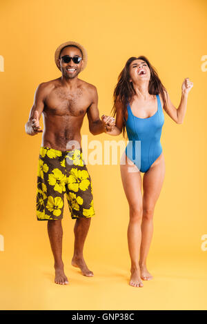 Young beautiful happy cheerful couple en tenant les mains de beachwear isolé sur fond orange Banque D'Images